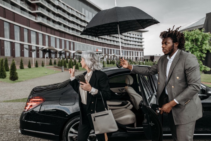 Driver holding an umbrella while a guest gets out of the black car in front of a hotel