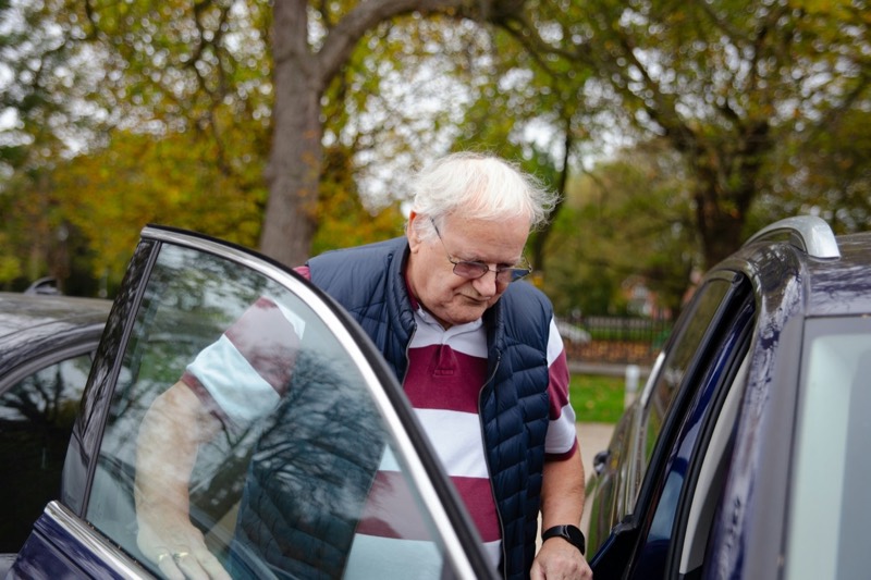 Older man carefully getting into a dark car
